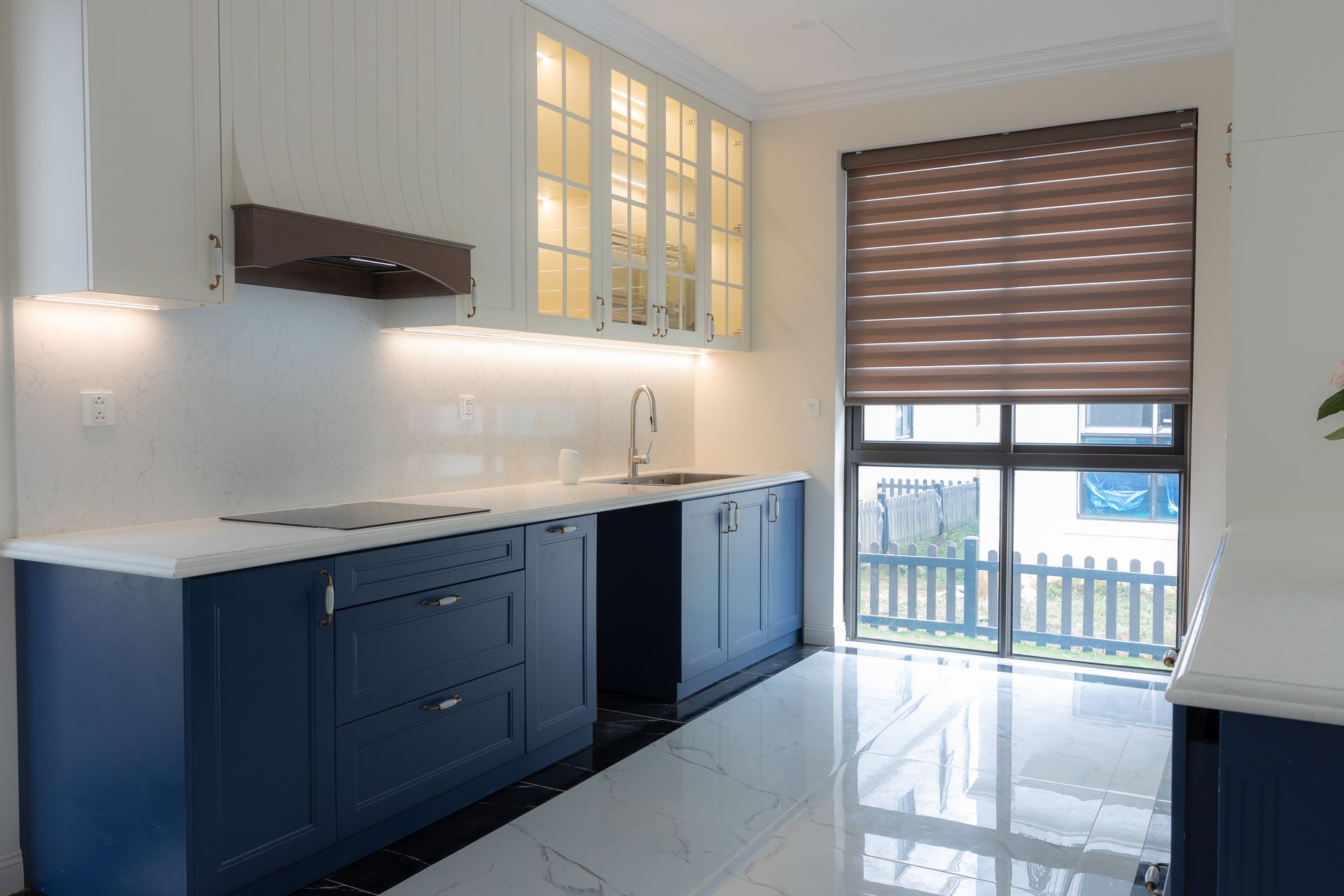 Bright modern kitchen featuring blue cabinetry, marble countertops, and ample natural light through large windows.