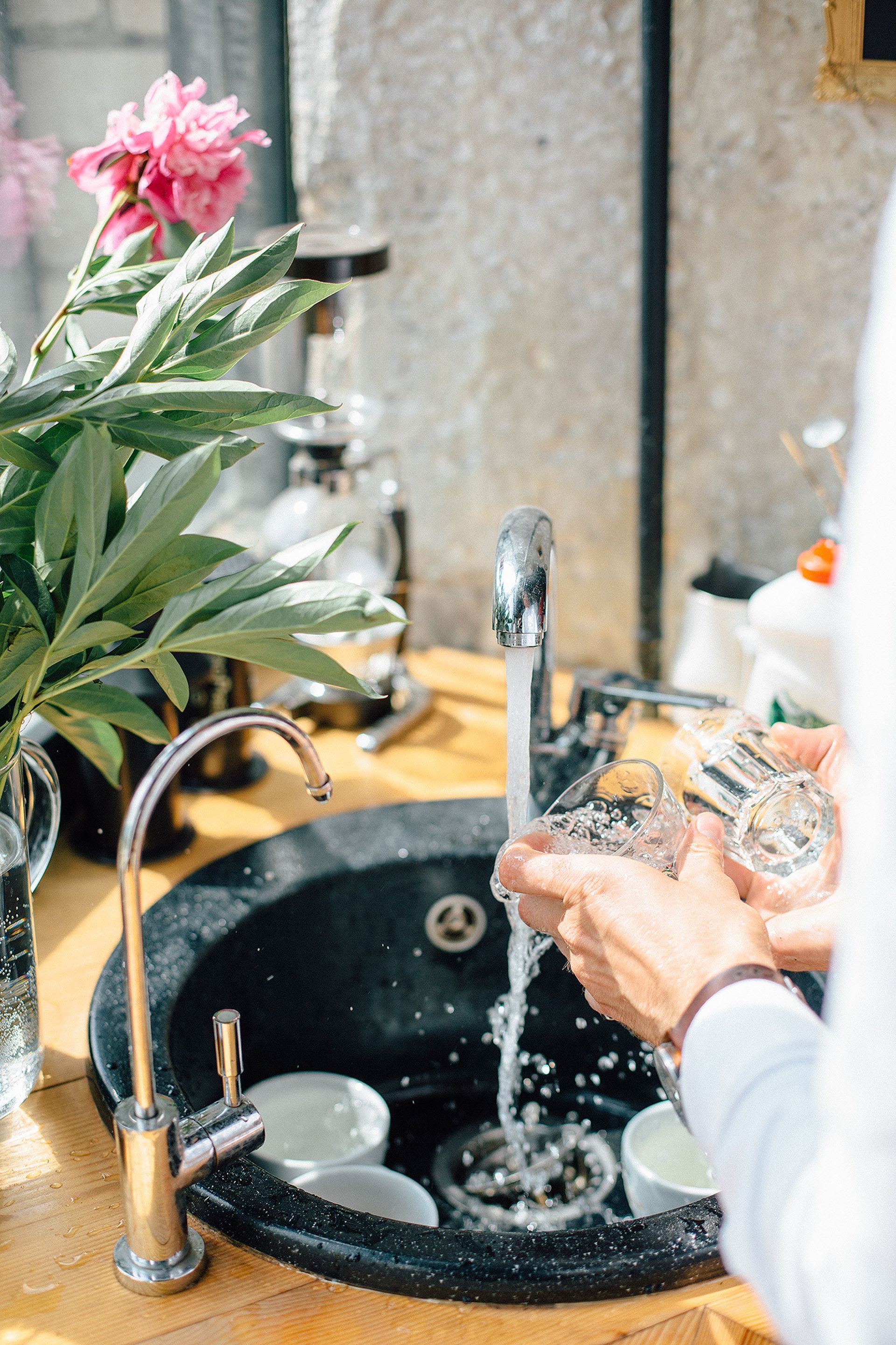 Bright kitchen scene with a person washing glasses by a sink, adorned with fresh flowers.