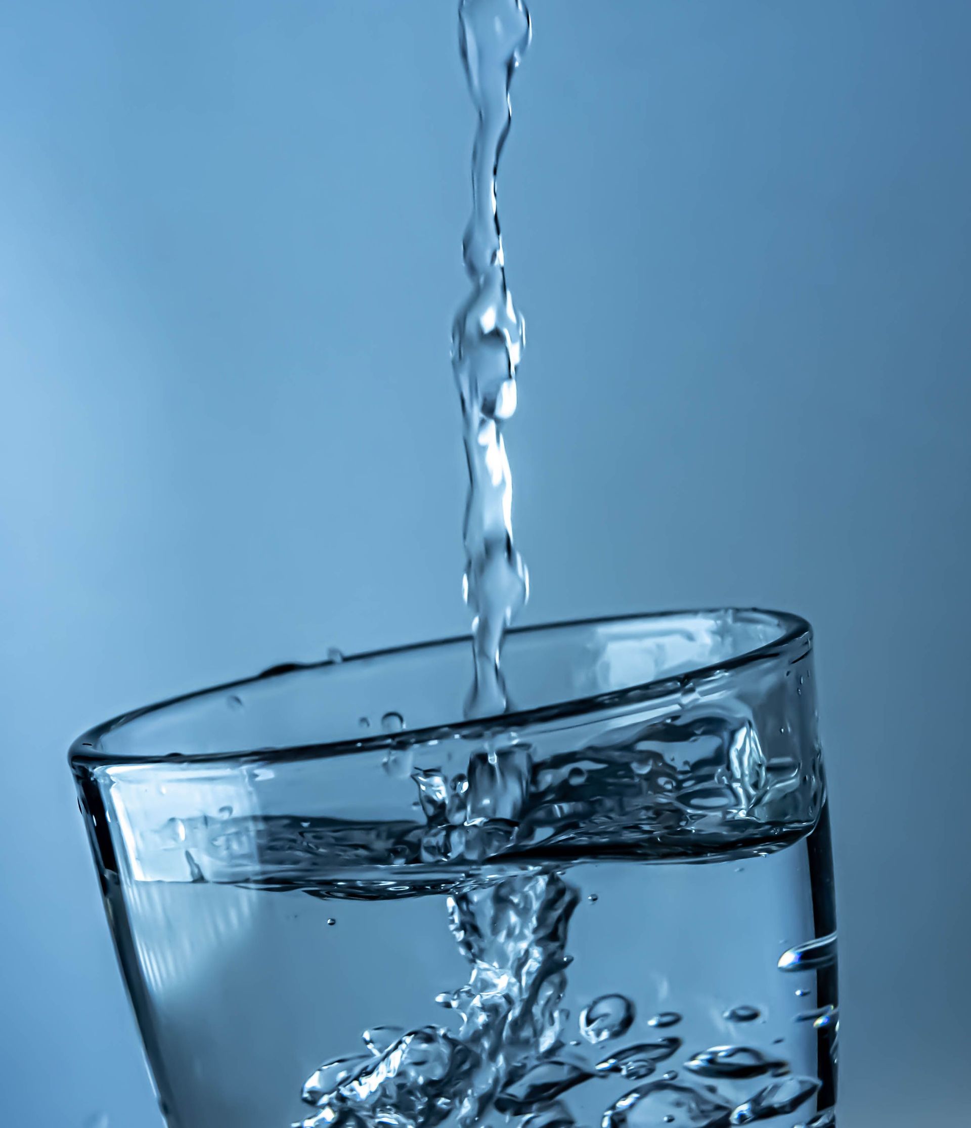 A close-up shot of water pouring into a clear glass, creating splashes.